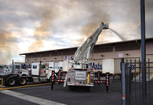 Photo taken on the Hulikoa Drive side of the Kohanaiki Business Park, as fire crews battle flames approaching the back of a building.