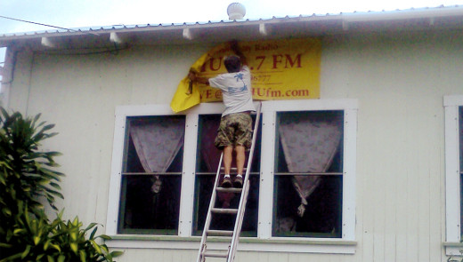 Mike McDonough, a local Pahala resident, assists in taking down the KAHU 91.7 FM station banner from the side of the building (June 2013, courest KAHU Radio) 