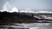 Fisherman pound the shoreline as high surf pounds Keaukaha