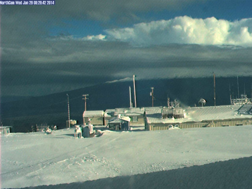 View looking north on Mauna Loa. The snow covered summit of Mauna Kea can be seen peeking through clouds in the distance. 