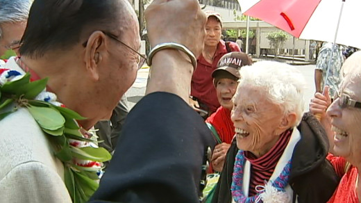 Saramae Landers, with daughter Sara Burgess by her side, chats with Senators Daniel Inouye (late) and Daniel Akaka  under  a sea of umbrellas in the Hilo rain (2010)