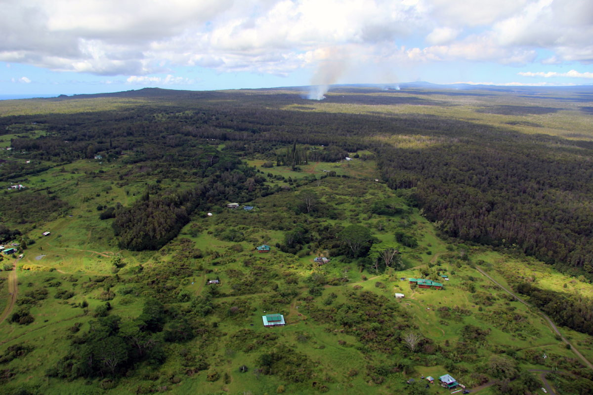 Kaohe Homesteads subdivision is seen at the bottom of this photograph. Puʻu ʻŌʻō is visible on the horizon in the upper right portion of the photograph. The flow is the smoke near the horizon. (USGS HVO)