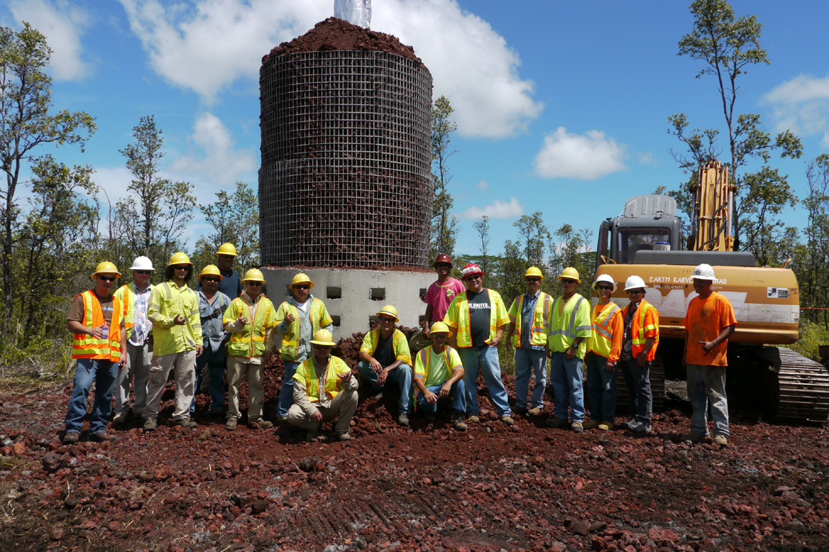 Photo by Hawai‘i Electric Light Company". HELCO employees install protection around a utility pole in the Puna area using heat resistant and dispersive material.