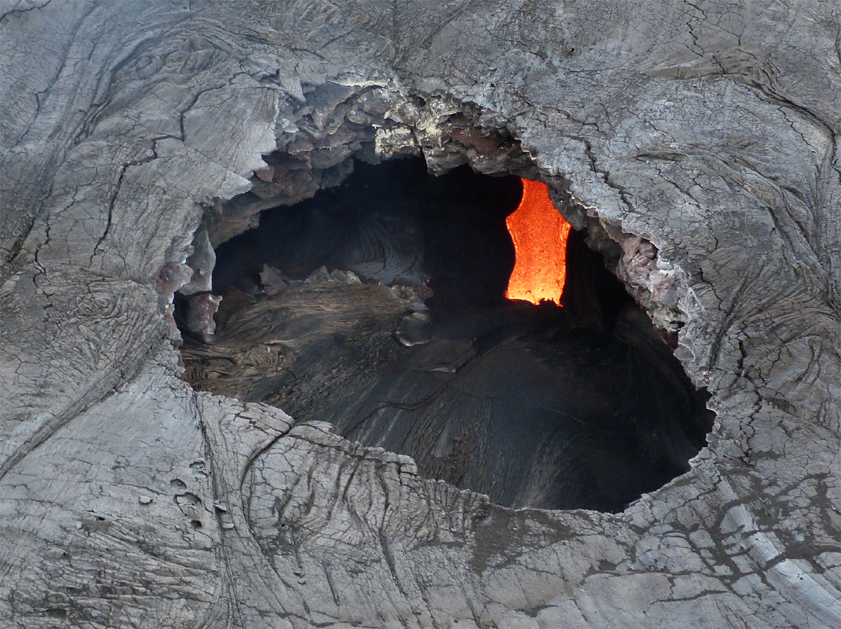 USGS HVO photo shows an aerial view into a skylight that reveals flowing lava in the main tube feeding the June 27th lava flow. The large opening is about 7 meters (7.5 yards) across.