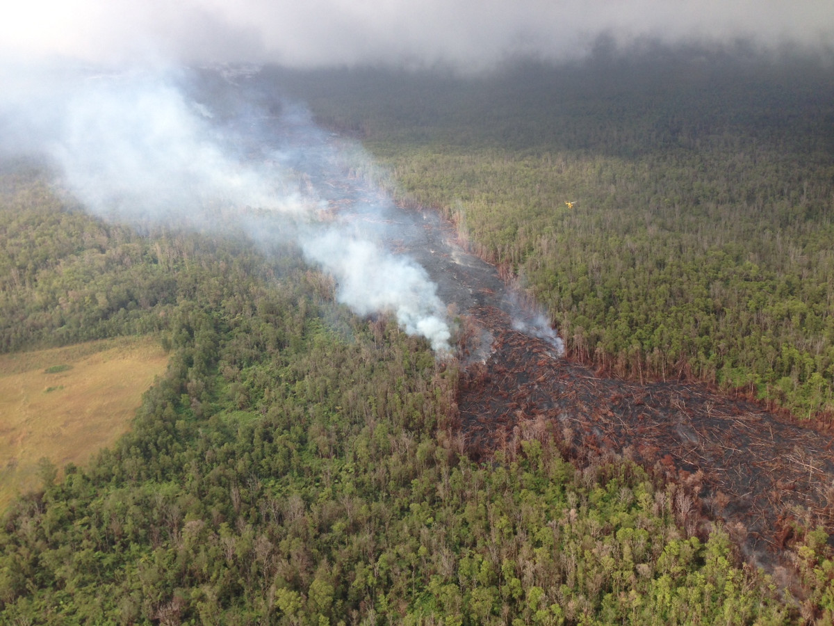 This photograph courtesy of Volcano Helicopters, taken before 11 am November 19, shows smoke from burning vegetation marking the edges of small breakouts from the June 27th lava-tube system north of the abandoned geothermal well site (middle left). This was the lowermost breakout as of Wednesday morning, located approximately 12 km (7.5 mi) straight line distance from Puʻu ʻŌʻō. Smoke and steam from breakouts upslope are also visible in the distance. Note yellow-colored helicopter for scale (middle right). 