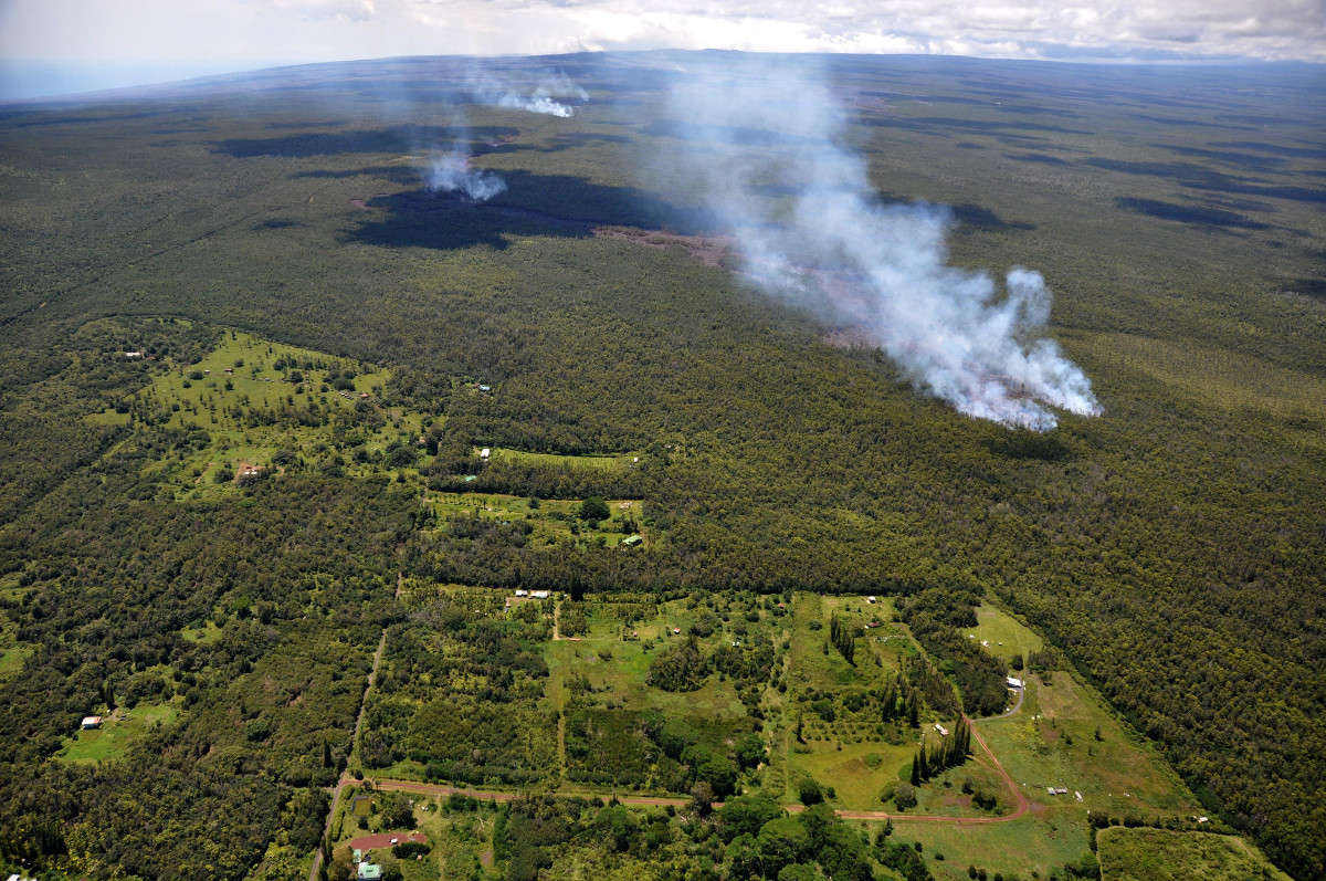 From September 4, 2014, to March 25, 2015, USGS Hawaiian Volcano Observatory scientists raised the Volcano Alert Level for Kīlauea from WATCH to WARNING as the June 27th lava flow advanced toward Pāhoa and posed an imminent hazard and threat to nearby communities and infrastructure.  Shown here on September 12, the leading edge of the lava flow (marked by dense smoke, middle right) burned through thick forest less than 200 m (220 yds) from the boundary of Kahoe Homesteads (lower left).  USGS photo.