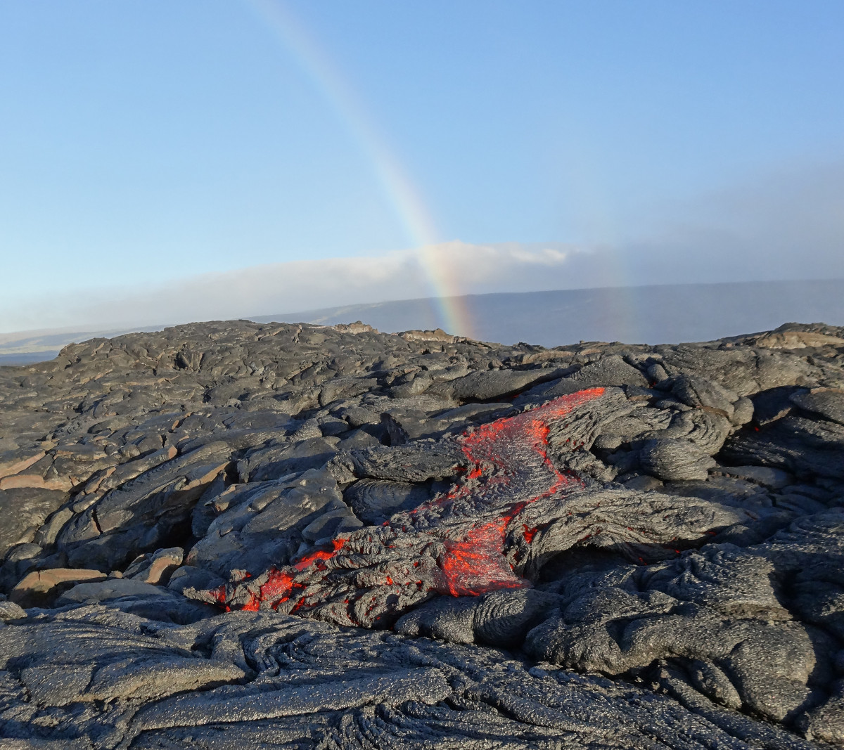 (USGS photo) A faint double rainbow provided a beautiful backdrop for sluggish pāhoehoe lava oozing out from near the flow front on the morning of July 22.