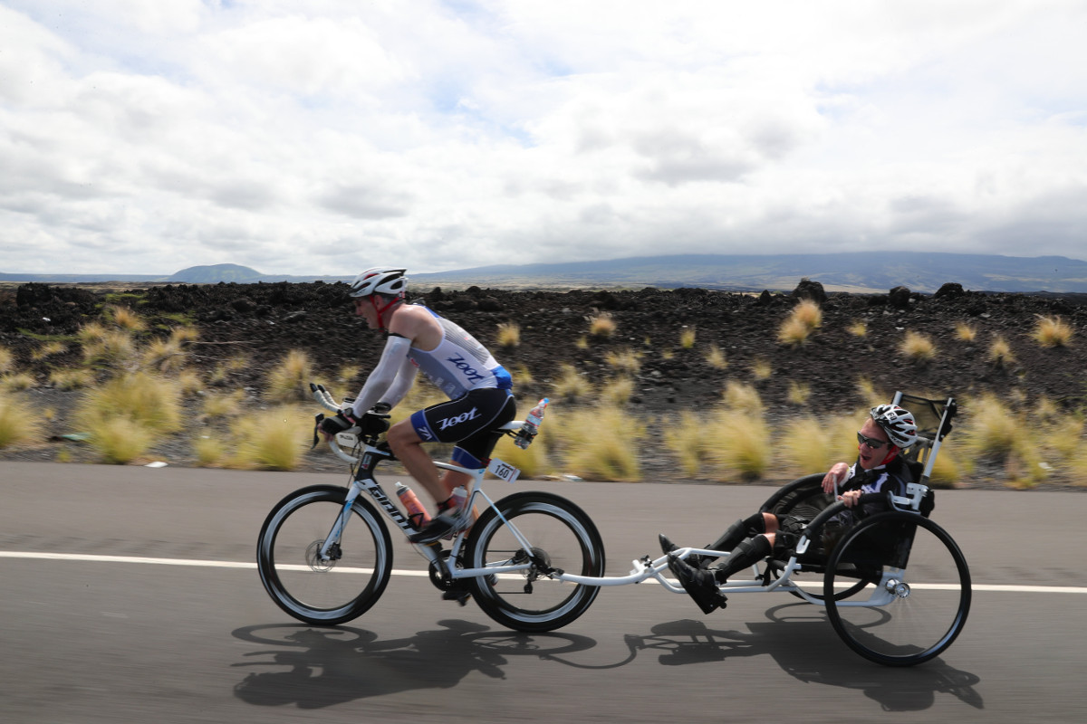 COURAGEOUS DUO. Inspiring people with their triumphant spirit, Jeff Agar pulls his son, Johnny, who suffers with cerebral palsy, along the bike course at the 2016 IRONMAN World Championship in Kailua-Kona, Hawai’i. (Tom Pentington/Getty Images for IRONMAN) - Copyright © 2016 IRONMAN
