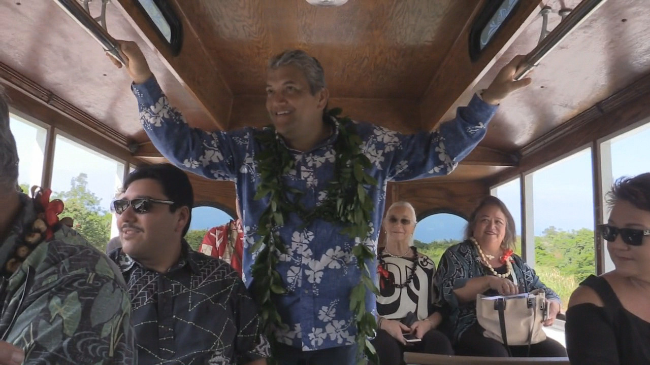 Mayor Kenoi smiles wide in the back of the trolley as it takes the first trip over the new bypass.