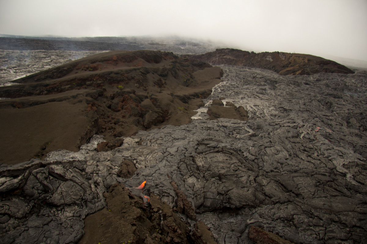 In this USGS photo of the breakout, a webcam , looking upslope toward Puʻu ʻŌʻō, is visible at the top of the cone near the upper right. Puʻu ʻŌʻō is shrouded by clouds in the background at the top of photo.